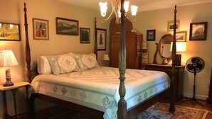 Un dormitorio con cama con dosel, candelabro, ventilador de pie y cómoda de madera.