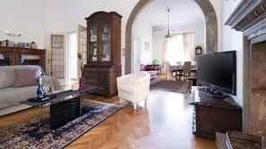 Un salón espacioso con suelo de madera, un amplio arco de entrada, un sillón blanco, una estantería, una chimenea y un televisor de pantalla plana.