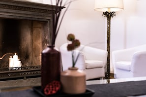 A fireplace with lit candles, a vase with dried flowers, and a modern floor lamp.