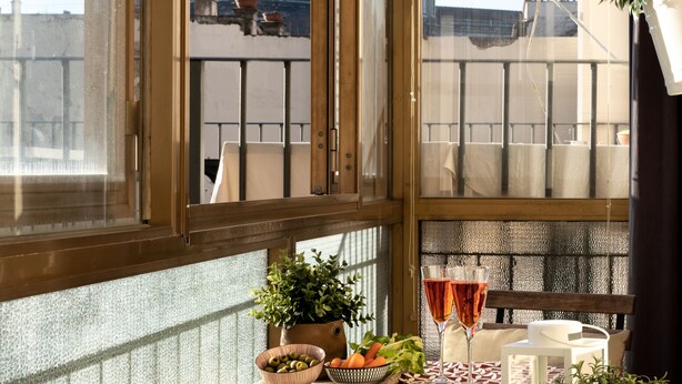Un balcón con una mesa para dos, una planta en maceta y vistas a una cúpula y edificios.