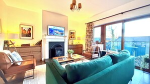 A living room with a sofa, armchair, fireplace, and large windows offering a view. - Harriet's Cottage. Chic & Cozy, Walk Everywhere! (Dingle)