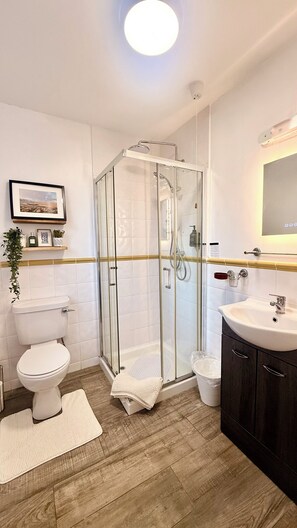 Une salle de bain moderne avec une douche à parois de verre, des toilettes blanches, un lavabo avec un miroir et un plancher en bois.