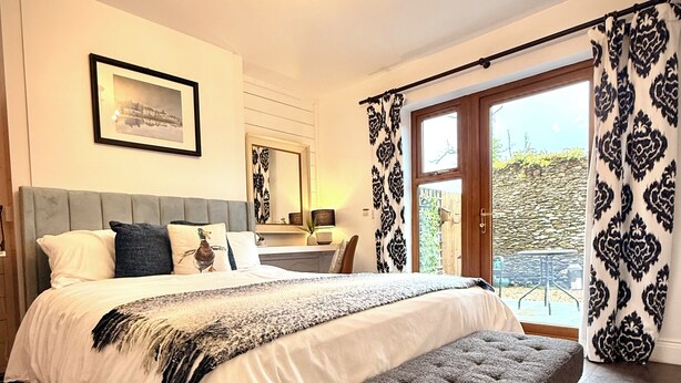 A bedroom with a large bed, a bench, a chandelier, a framed picture, and a view through the window. - Harriet's Cottage. Chic & Cozy, Walk Everywhere! (Dingle)