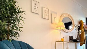 A room with a blue armchair, a wooden floor, a lamp, a mirror, and framed certificates on the wall. - Harriet's Cottage. Chic & Cozy, Walk Everywhere! (Dingle)