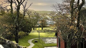 A rural landscape with a clear path leading through a grassy area, surrounded by leafless trees and a distant view of a village. - Harriet's Cottage. Chic & Cozy, Walk Everywhere! (Dingle)