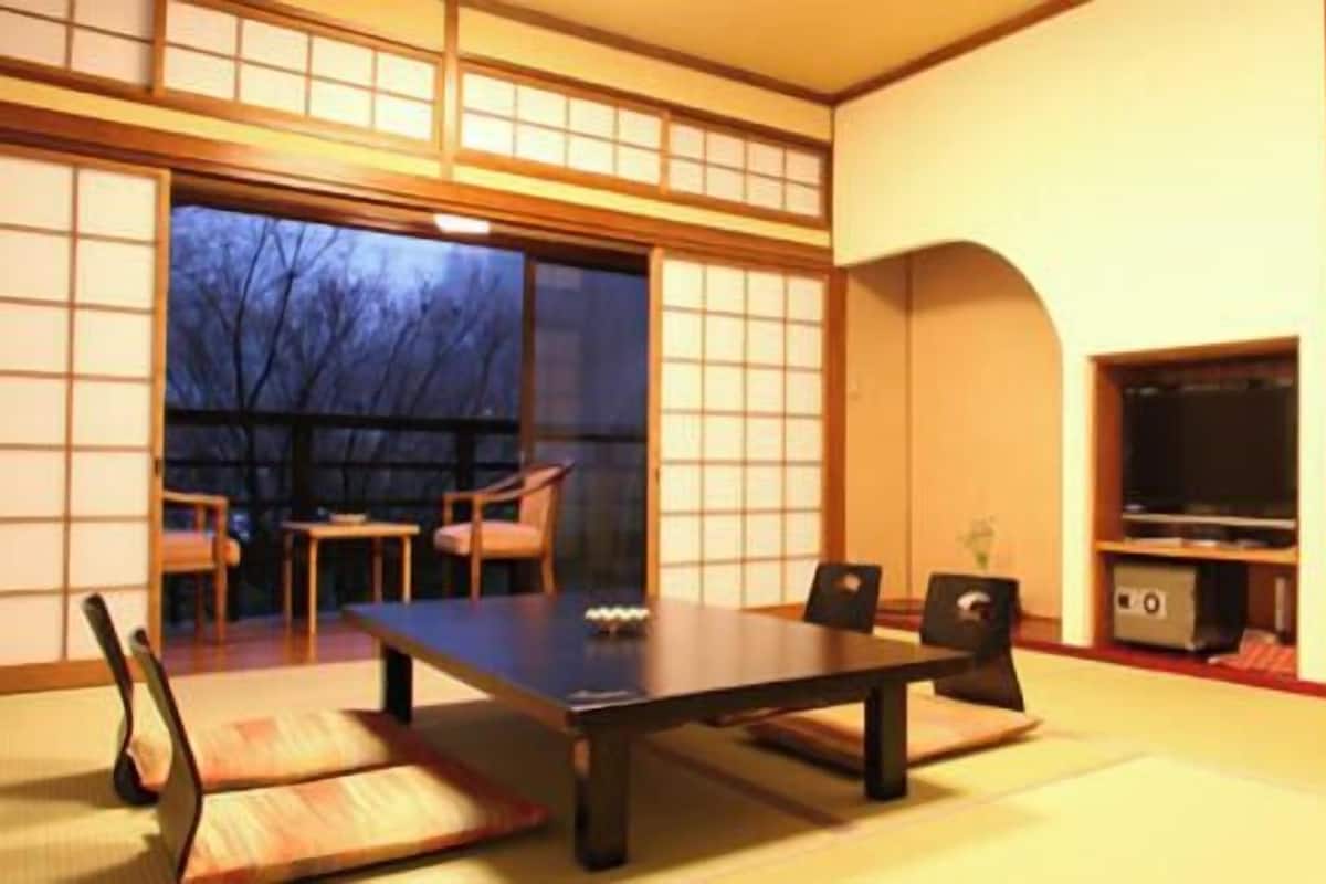 A traditional Japanese-style room with tatami flooring, a low table, chairs, a television, and sliding doors.