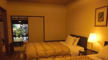 Habitación de hotel con dos camas, una mesita de noche con lámpara y vistas a un área exterior con mesas y sillas.