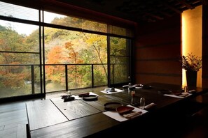 A dining area with a large window overlooking a forested area with autumn foliage. - Kurokawa Onsen Yumerindo (Minamioguni)