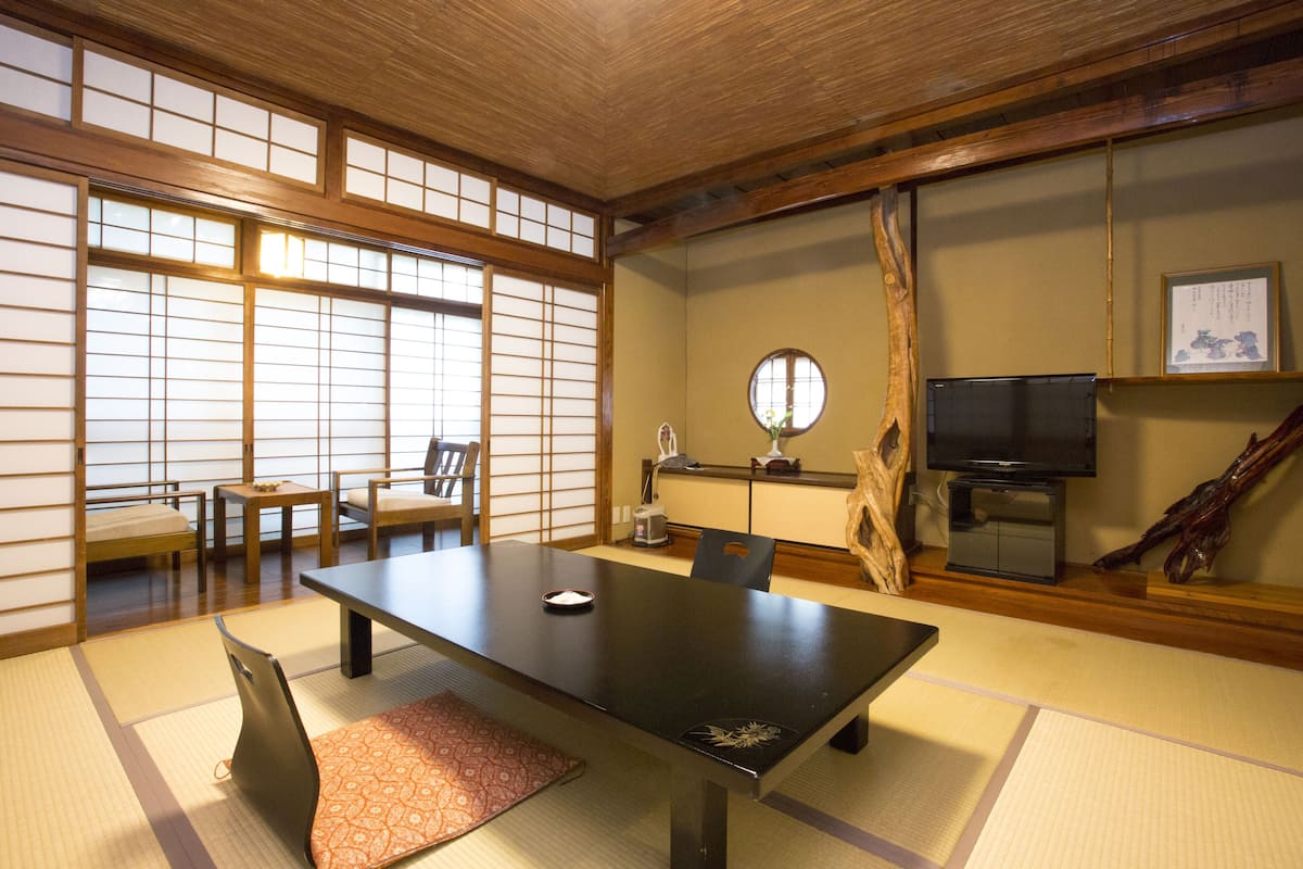 A traditional Japanese room with tatami flooring, a low table with cushions, a television, and a wooden cabinet.