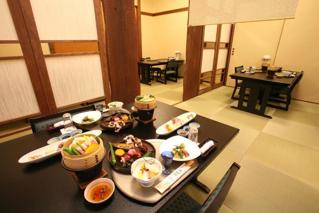 A traditional Japanese dining room with tatami flooring, low tables, and a variety of dishes on a central table.