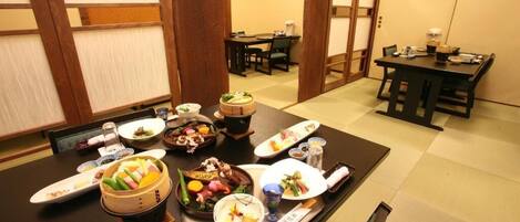 A traditional Japanese dining room with tatami flooring, low tables, and a variety of dishes on a central table.