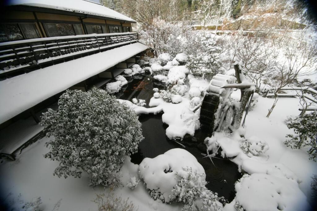 Un espace extérieur enneigé comprenant une petite cascade, un pont et un bâtiment à l’architecture traditionnelle.