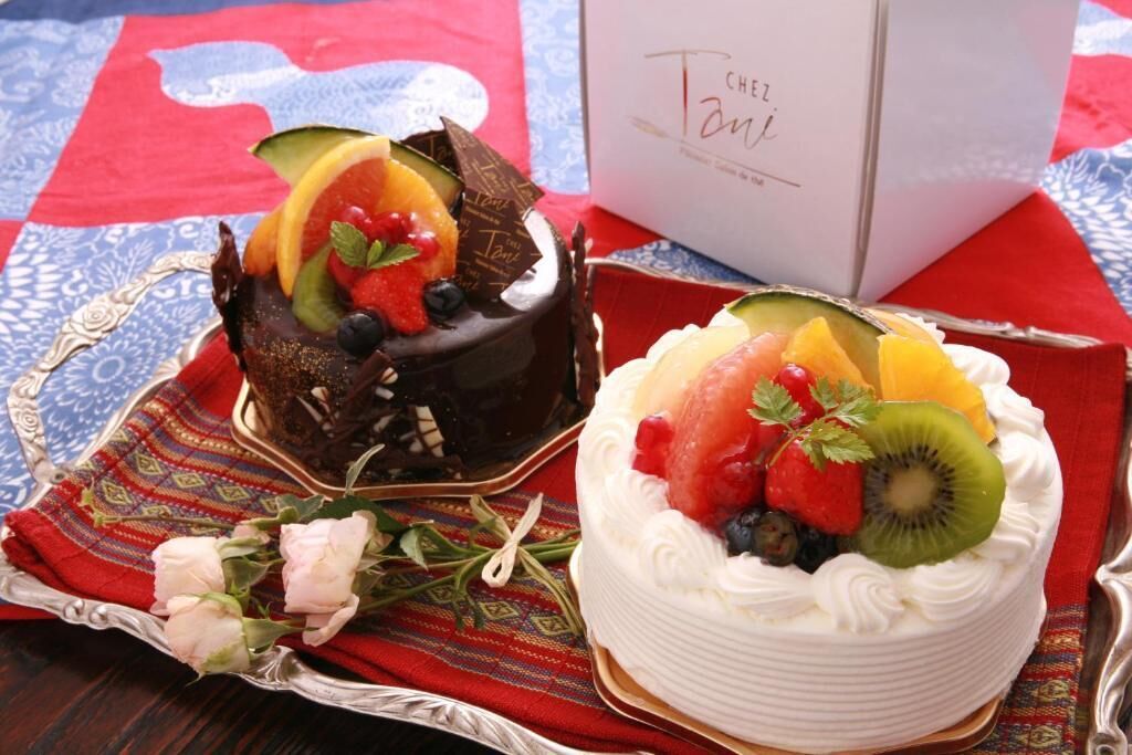 Two cakes on a table with a patterned cloth and a white box in the background.