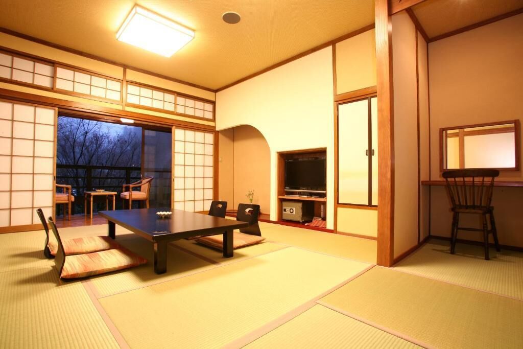 A traditional Japanese room with tatami flooring, a low table, chairs, a television, and sliding doors.