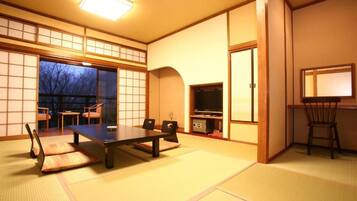 A traditional Japanese room with tatami flooring, a low table, chairs, a television, and sliding doors.