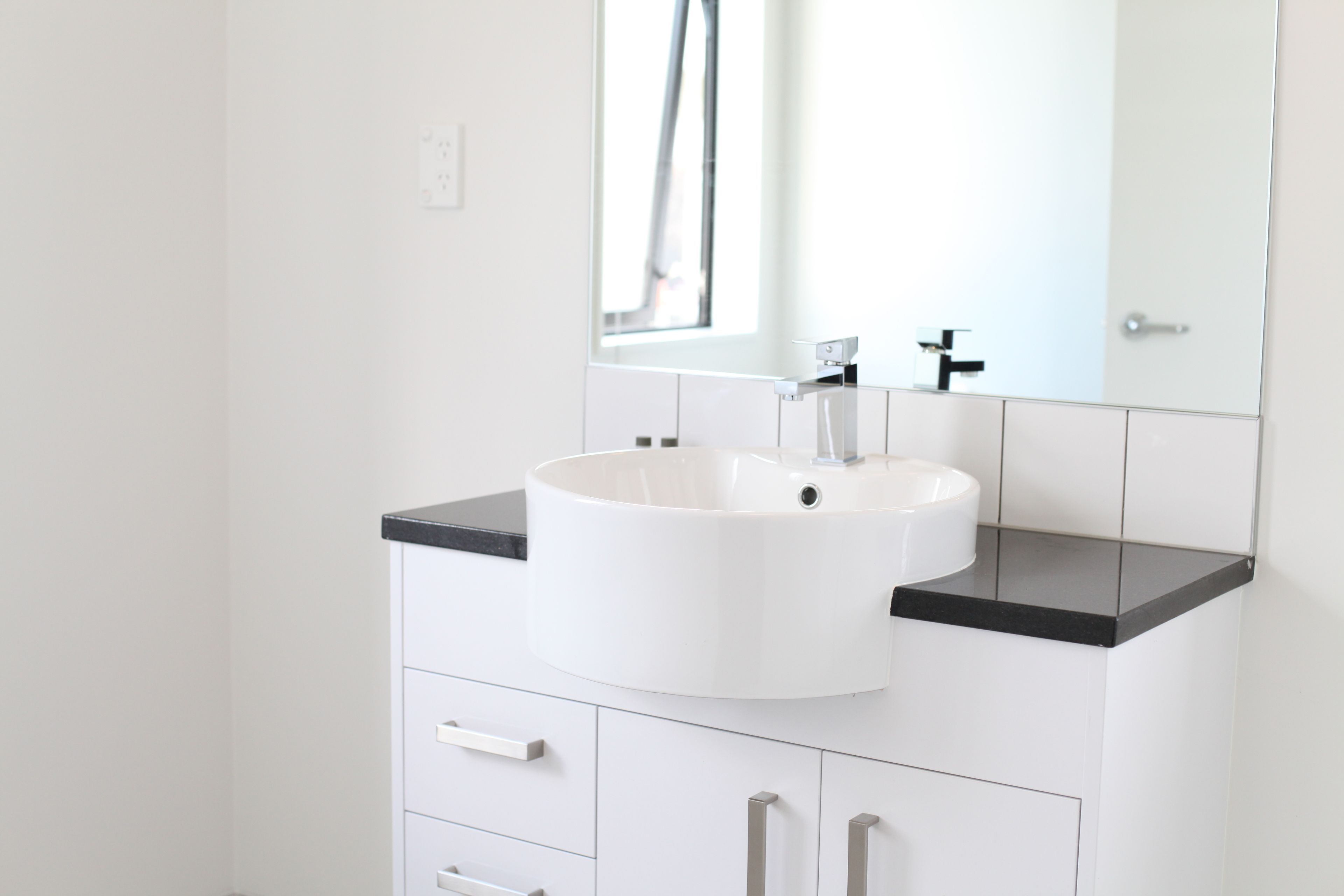 Un baño moderno con un lavamanos blanco, encimera negra y un espejo grande encima.