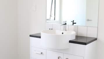 Un baño moderno con un lavamanos blanco, encimera negra y un espejo grande encima.