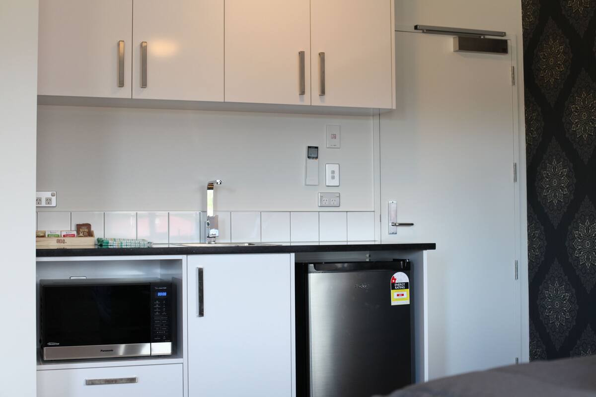 Una cocina compacta con armarios blancos, microondas y refrigerador.