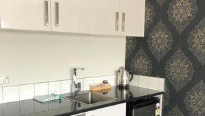 Eine kompakte Küche mit weißen Schränken, einer schwarzen Arbeitsplatte, einer Edelstahl-Spüle und einem schwarzen Kühlschrank.