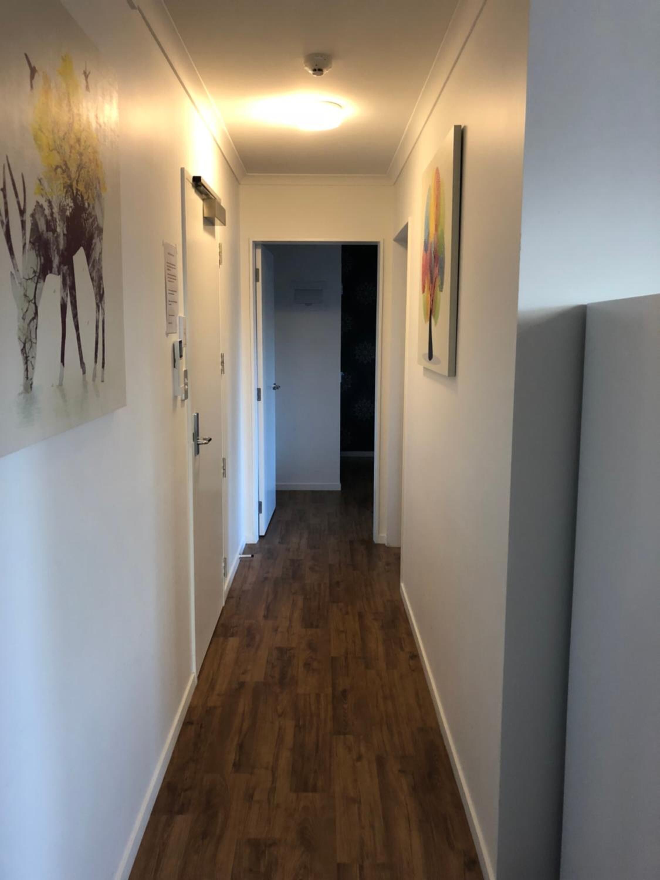 Un couloir doté d’un plancher en bois, de murs blancs et d’œuvres d’art.