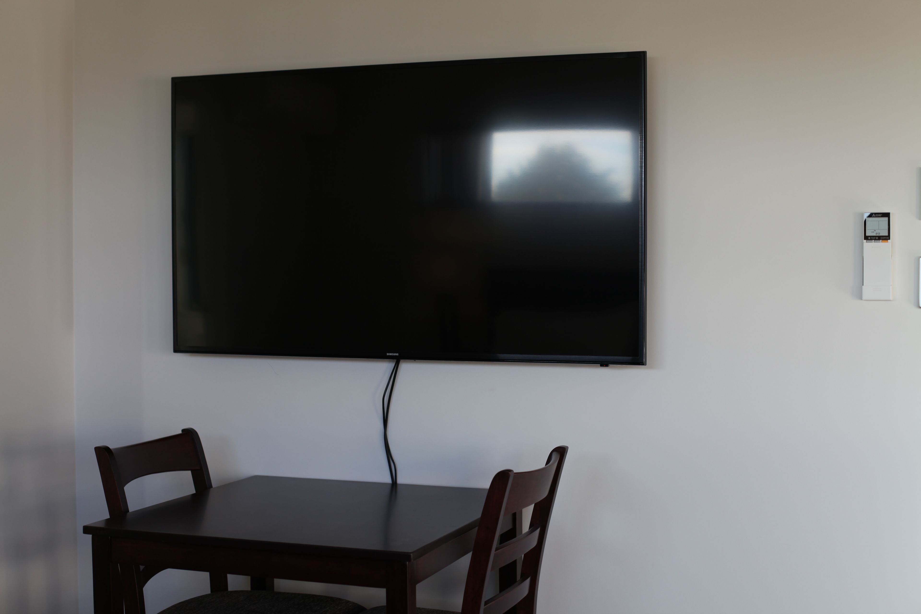 A room with a flat-screen TV mounted on the wall, a wooden table, and two chairs.