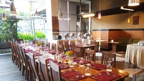 A restaurant with a long wooden table set for dining, surrounded by chairs. - Bali World Hotel (Bandung)