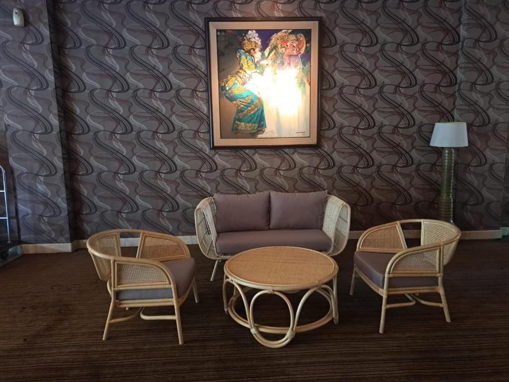 Une pièce avec un papier peint à motifs, un canapé, deux fauteuils en osier, une table ronde et une œuvre d’art encadrée accrochée au mur.