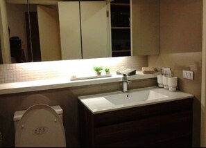 A modern bathroom with a white sink, a mirror above it, and a toilet. There is a small plant on the sink counter. - The Lake 3 Condominium (Pak Kret)