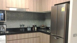 A modern kitchen with wooden cabinets, a black countertop, and a stainless steel refrigerator. - The Lake 3 Condominium (Pak Kret)