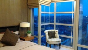 A hotel room with a large window, a bed, a chair, a nightstand, and a lamp. - The Lake 3 Condominium (Pak Kret)