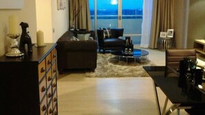 A living room with a sofa, a coffee table, and a view of the ocean through large windows. - The Lake 3 Condominium (Pak Kret)