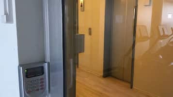 An elevator with a keypad and a digital display, a wooden floor, and a wall-mounted light fixture.