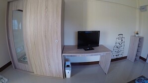 Una habitación con un armario de madera, un escritorio con computadora y un mueble bajo con cajones.