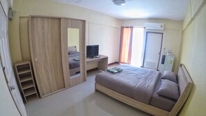 Un dormitorio con cama, televisor sobre un mueble, armario, espejo y dispensador de agua.