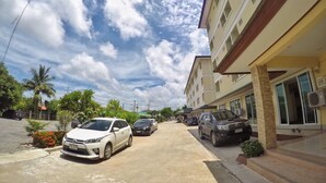 Vista de la calle con coches aparcados, un edificio con balcones y cielo despejado.