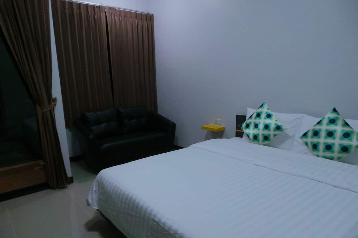 A hotel room with a bed, a chair, a nightstand, and a curtain.