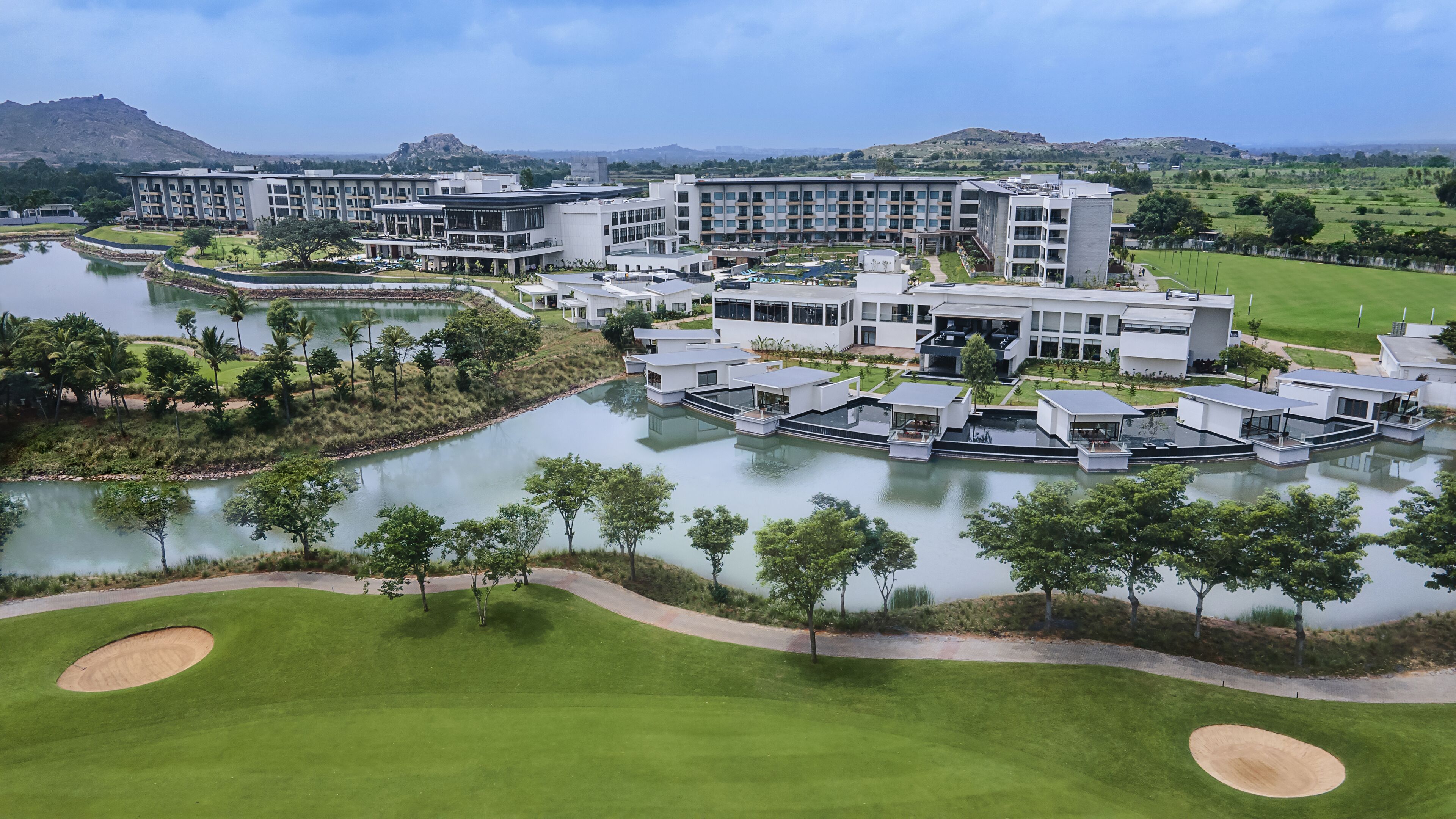 A modern resort with multiple buildings, a central water feature, and surrounding greenery.