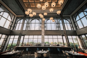 A spacious bar area with high ceilings and large windows, offering views of the outdoors.