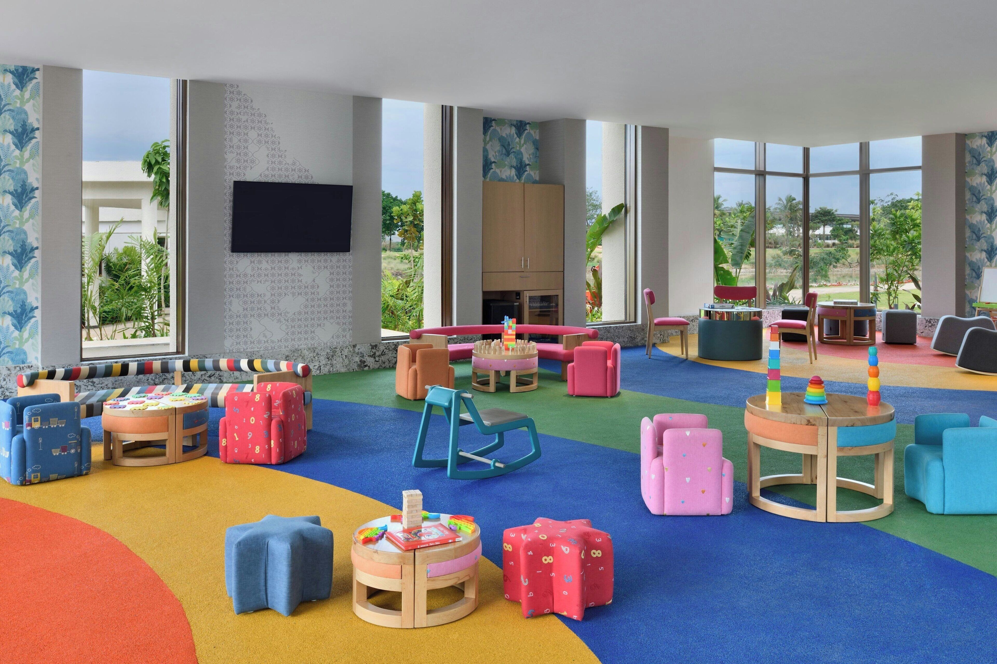 A children's play area with colorful furniture and large windows offering a view of greenery.