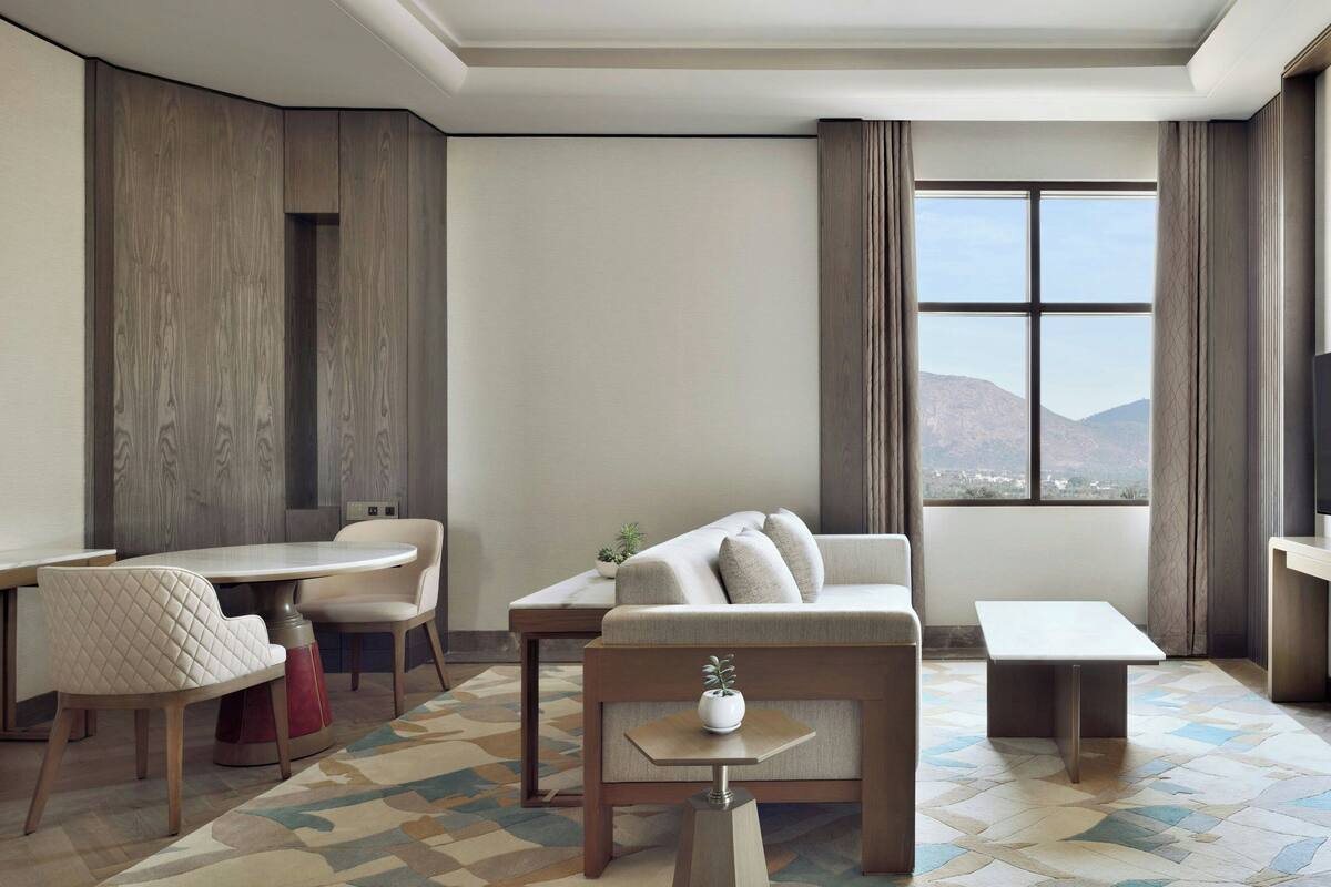 A modern living room with a sofa, chairs, a dining table, and a view of mountains through a large window.