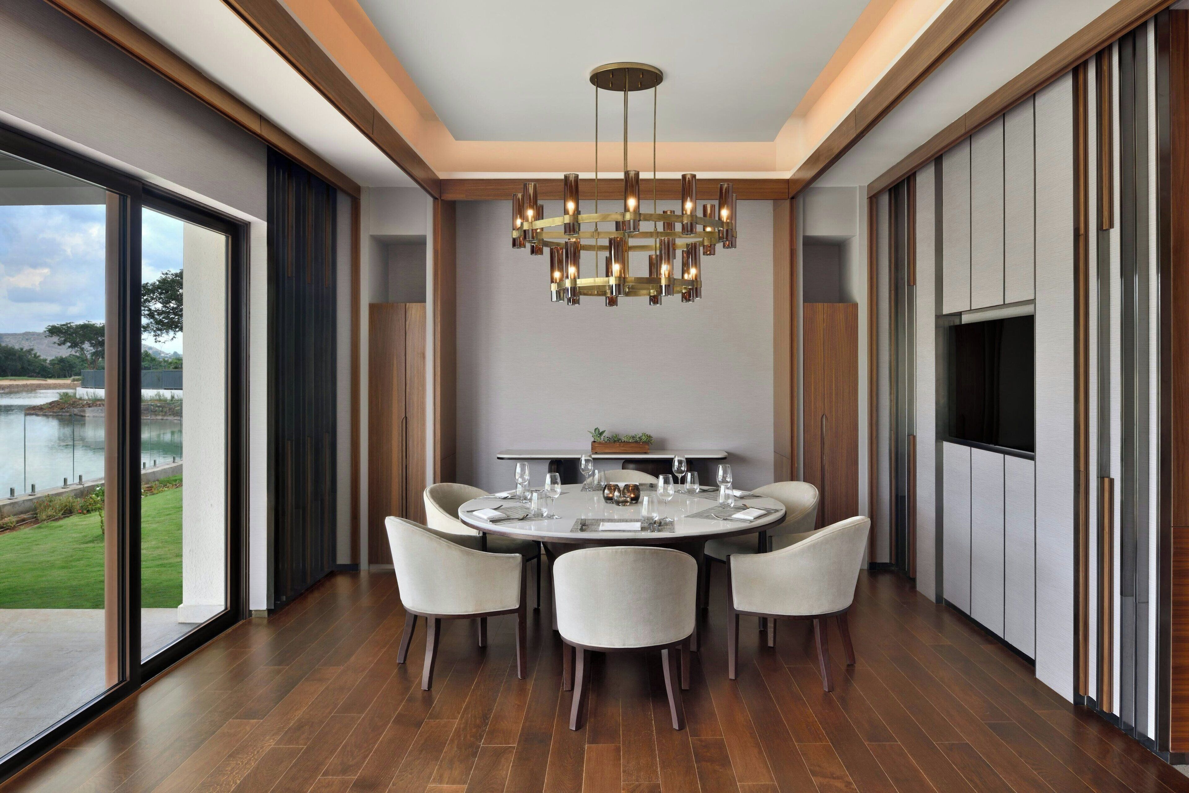 A modern dining area with a round table, six chairs, and a chandelier.