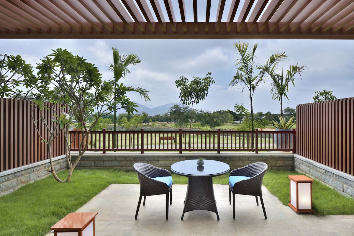 An outdoor patio with a round table and two wicker chairs, surrounded by a wooden pergola and a stone wall.