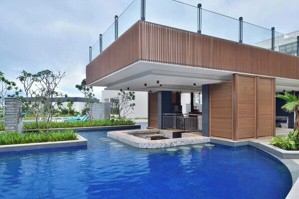 Un área de piscina moderna con una terraza de madera y sillones de descanso.