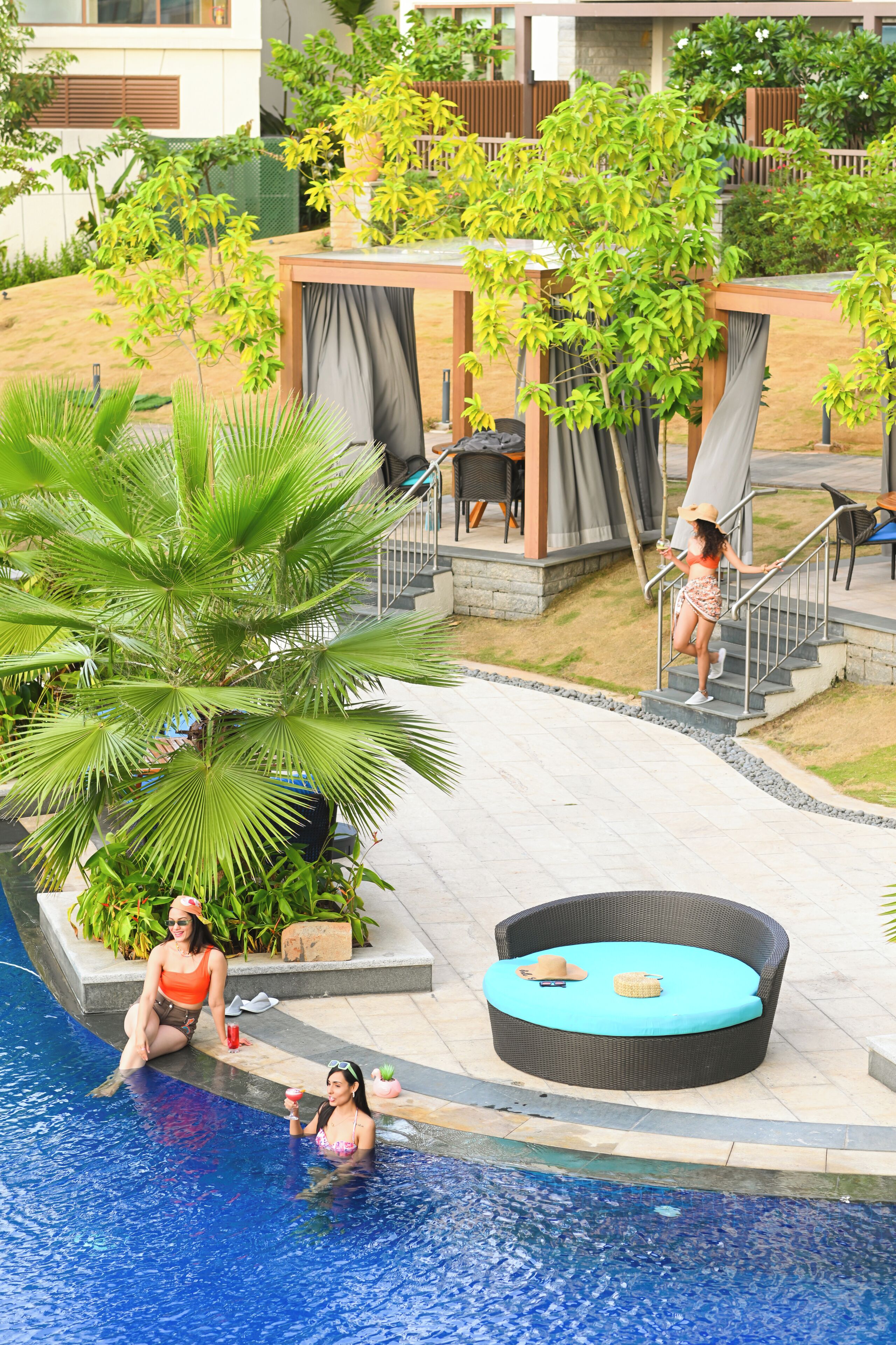 Un área de piscina con una silla de descanso, una palmera y una zona de estar cubierta.