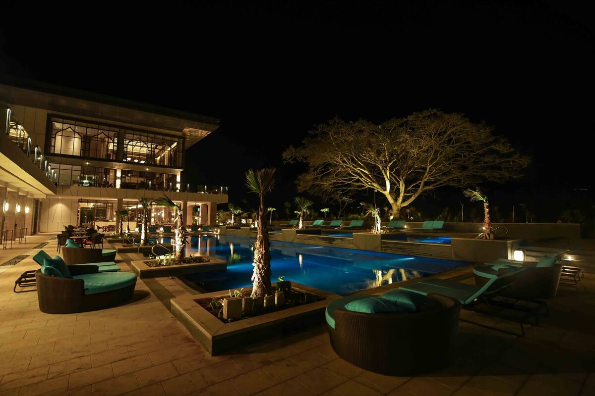 A nighttime pool area with lounge chairs and a large tree.