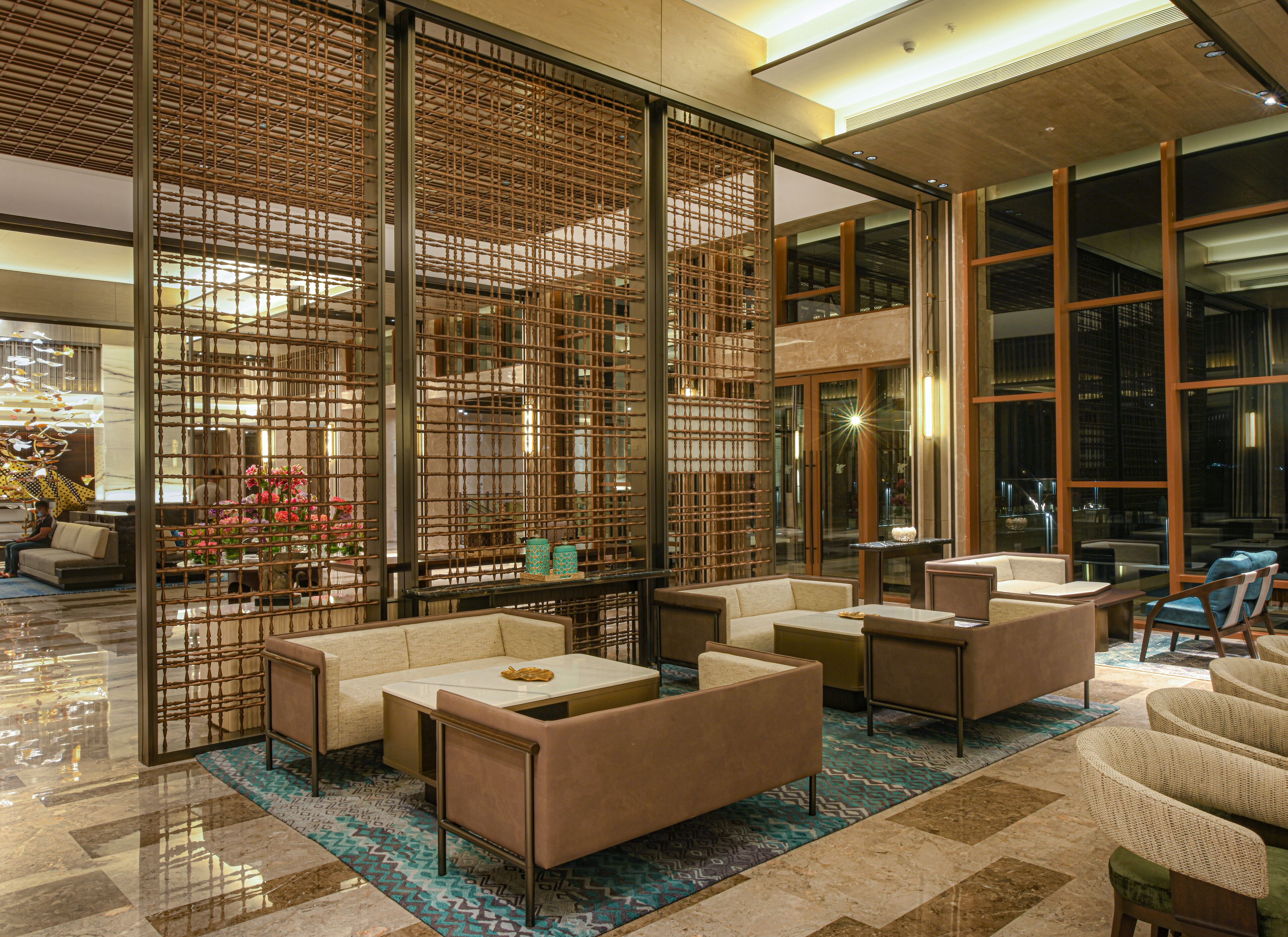 A modern lobby with seating areas, a decorative bamboo screen, and large windows offering views of the city.
