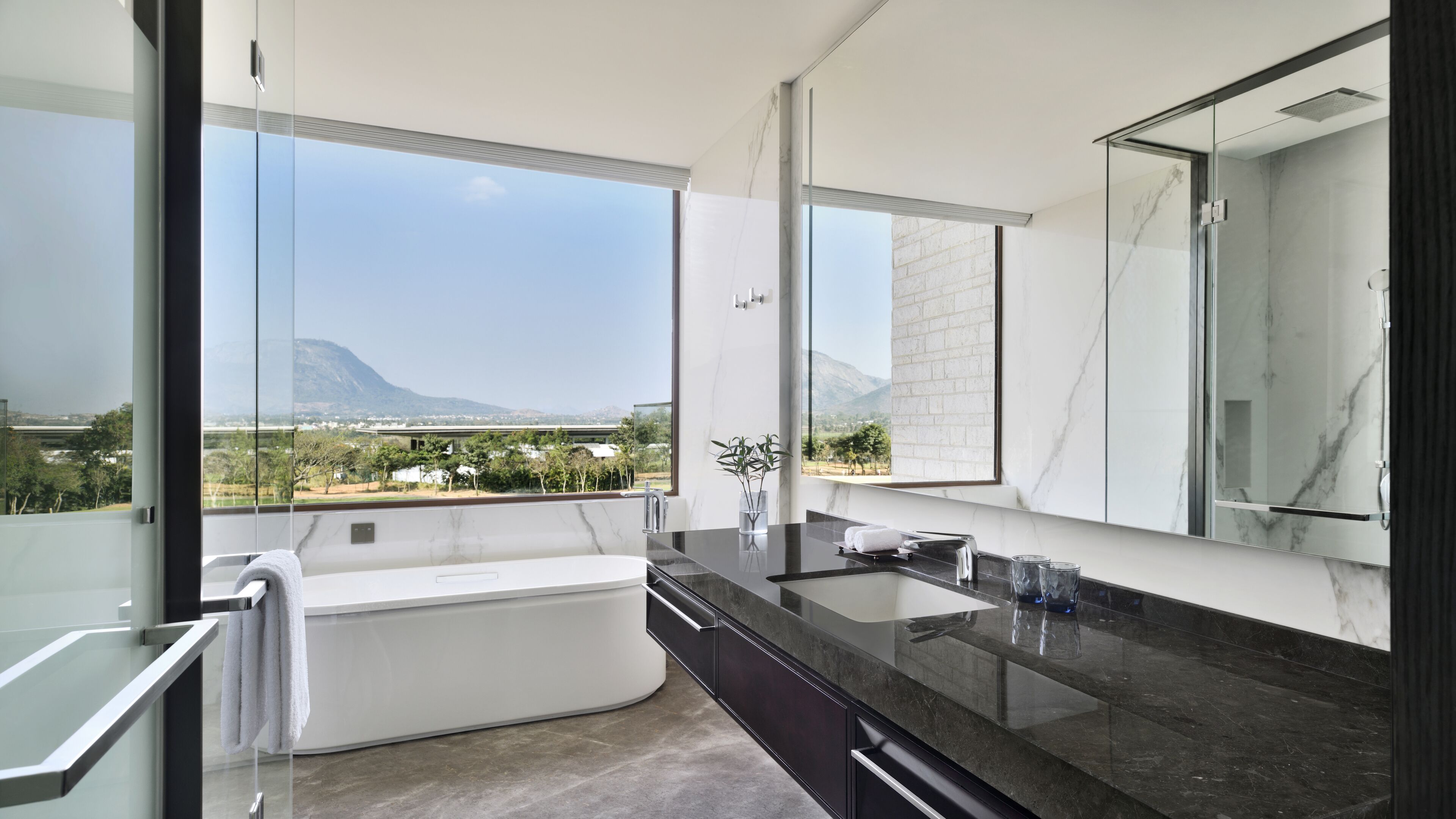 Un baño moderno con un espejo grande, una bañera y vistas a un paisaje montañoso.