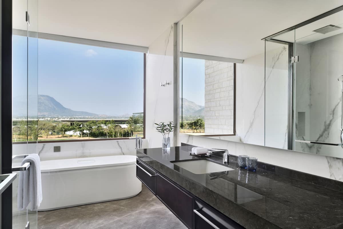 A modern bathroom with a large mirror, a bathtub, and a view of a mountainous landscape.