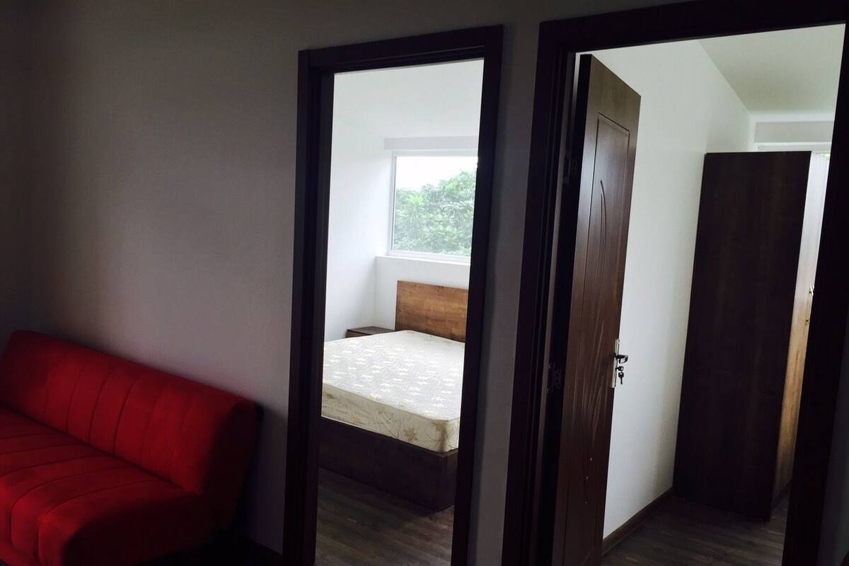 Una habitació amb un sofà vermell, un llit amb capçalera de fusta i una finestra.