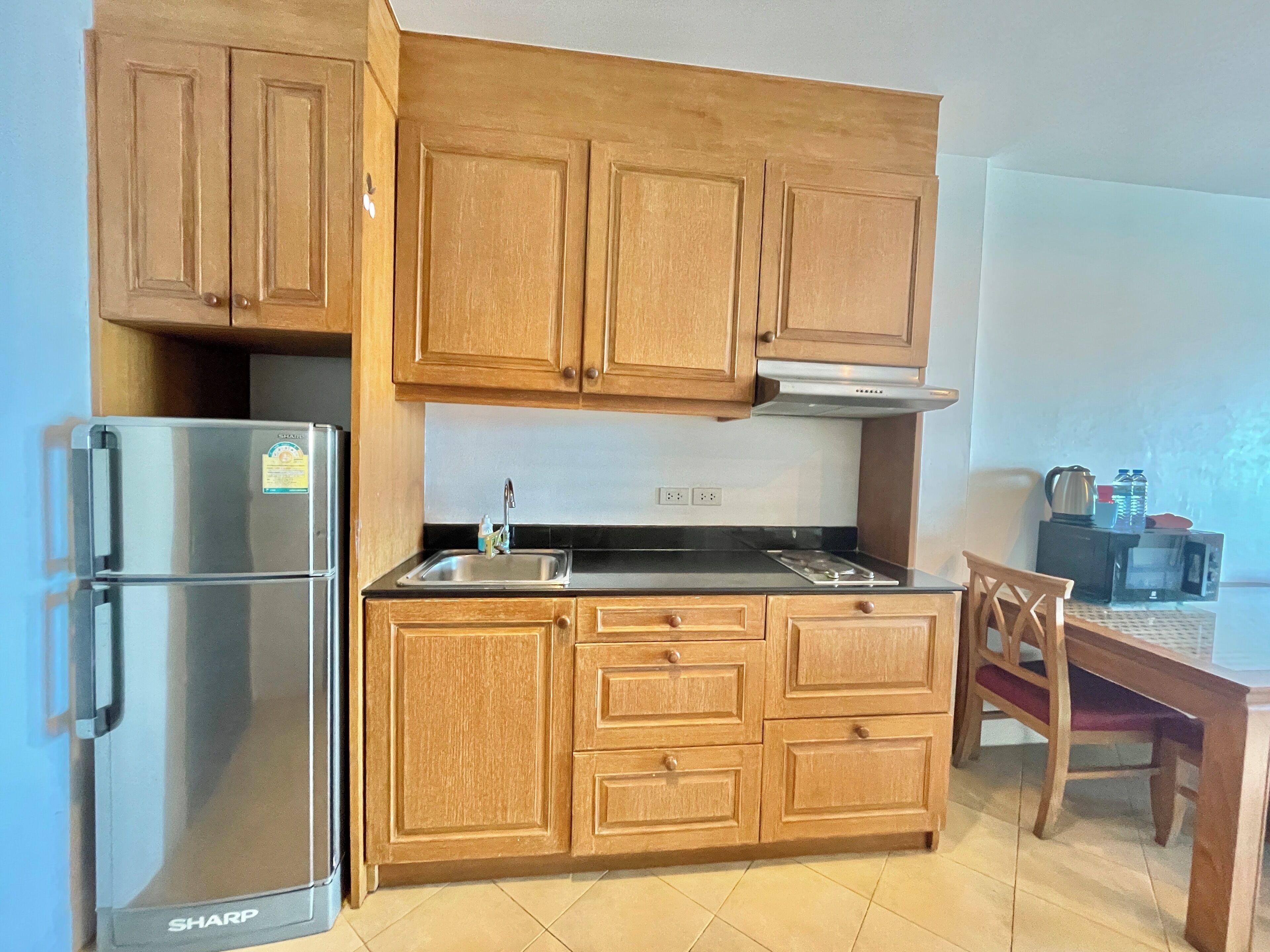Una cocina compacta con gabinetes de madera, un refrigerador de acero inoxidable, una estufa a gas y una mesa de comedor con sillas.